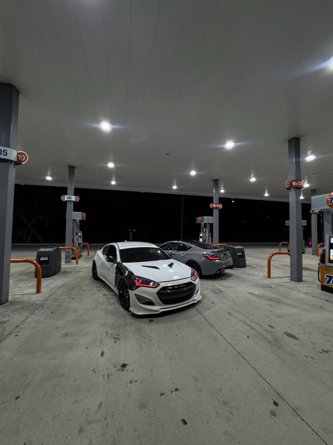 A modified Genesis coupe parked at night with city lights and reflections in the background.