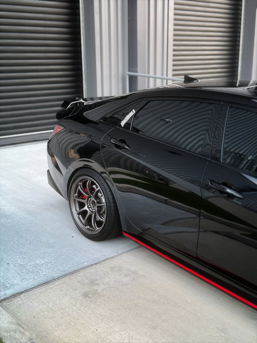 A black Hyundai Elantra N photographed from the rear-side angle outside a building with dark roller doors.