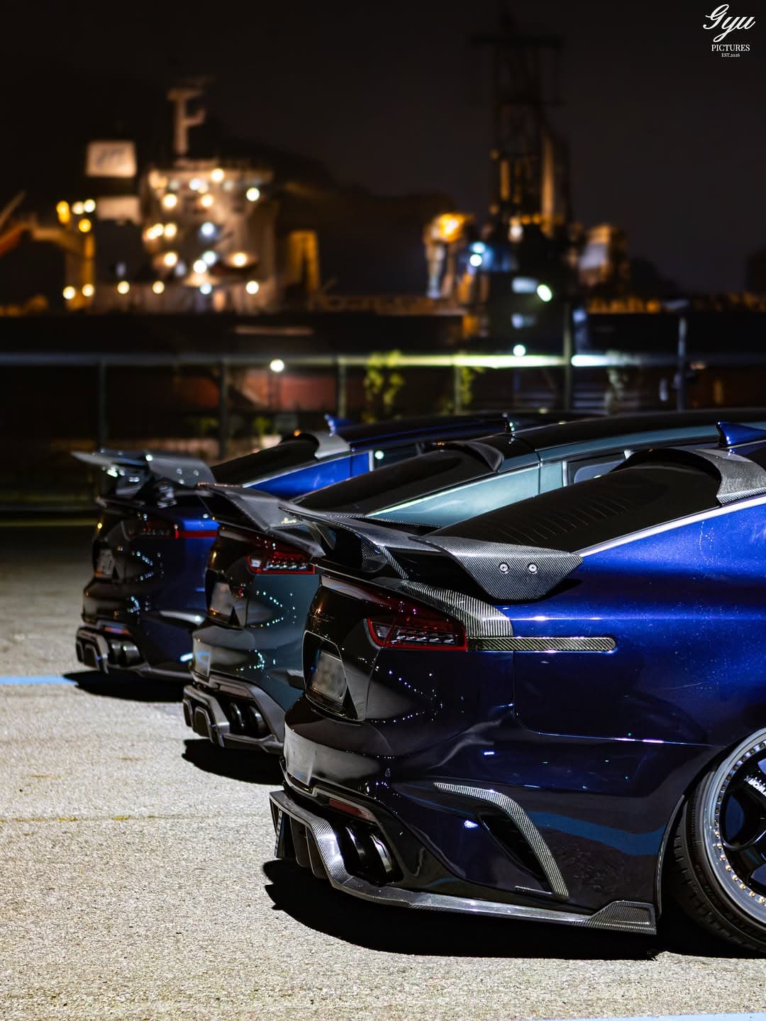A row of modified Kia Stingers photographed at night with the rear wings and body lines emphasized.
